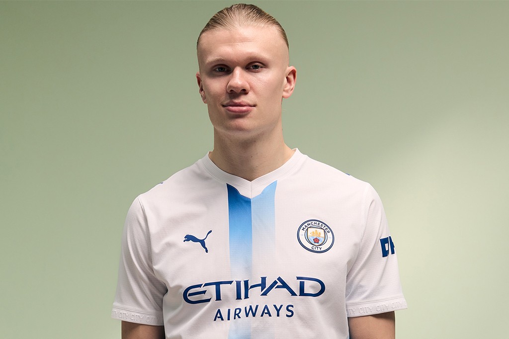 Jogador de futebol Erling Haaland, loiro de cabelo penteado para trás, veste a camisa branca do Manchester City com detalhes azuis e o logo Etihad Airways